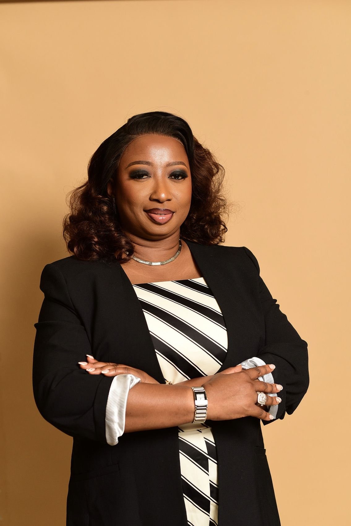 Kemi Sola-Popoola in a black blazer, arms folded, smiling